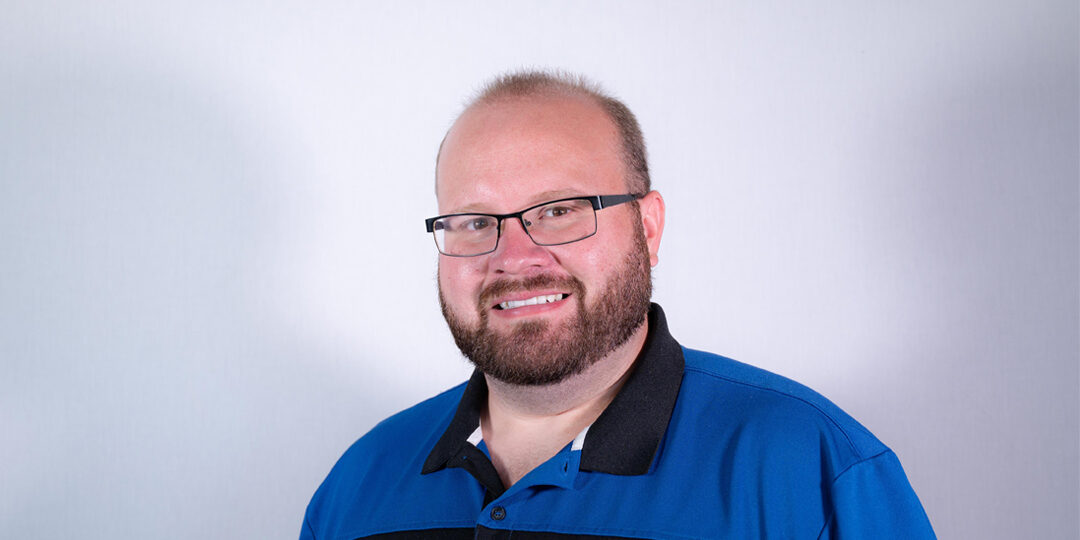 Headshot of man with glasses and blue and black hair in studio lighting