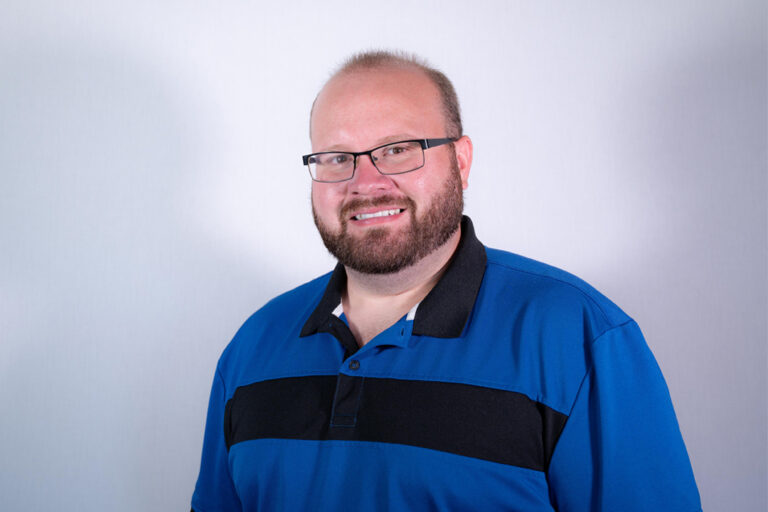 Headshot of man with glasses and blue and black hair in studio lighting