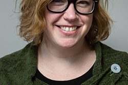 Woman smiling with short blonde hair and black glasses