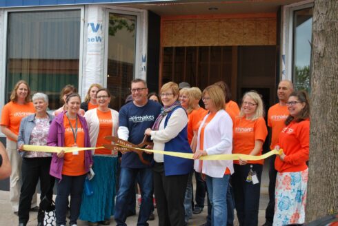 Staff members wearing orange holding a yellow ribbon and one woman cutting it with large scissors