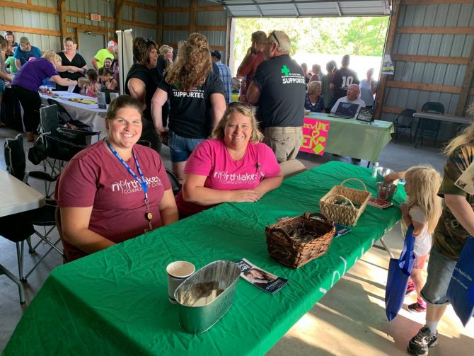 Two women in NorthLakes shirts sitting at a table handing out resources