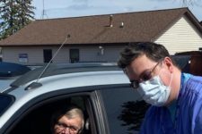 Man with scrubs and surgical max next to patient in their car