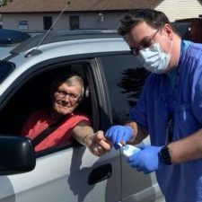 Curbside3-225×300 Man with scrubs and surgical max next to patient in their car