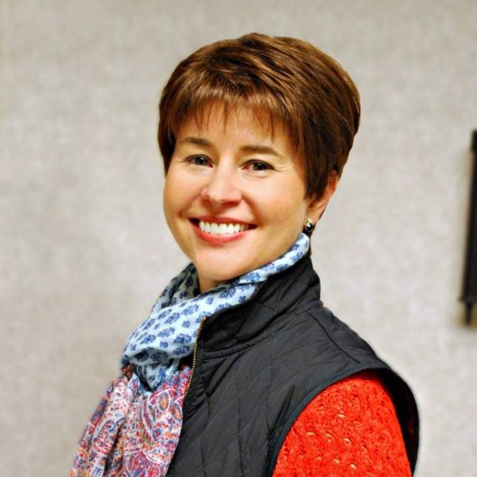 Woman with short brown hair smiling with scarf and vest on