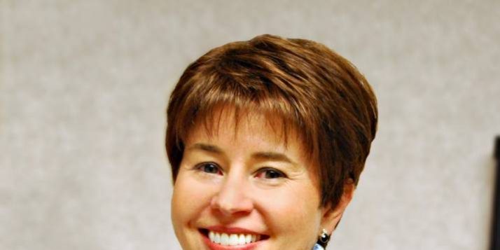 Woman with short brown hair smiling with scarf and vest on