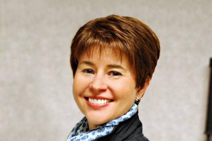 Woman with short brown hair smiling with scarf and vest on