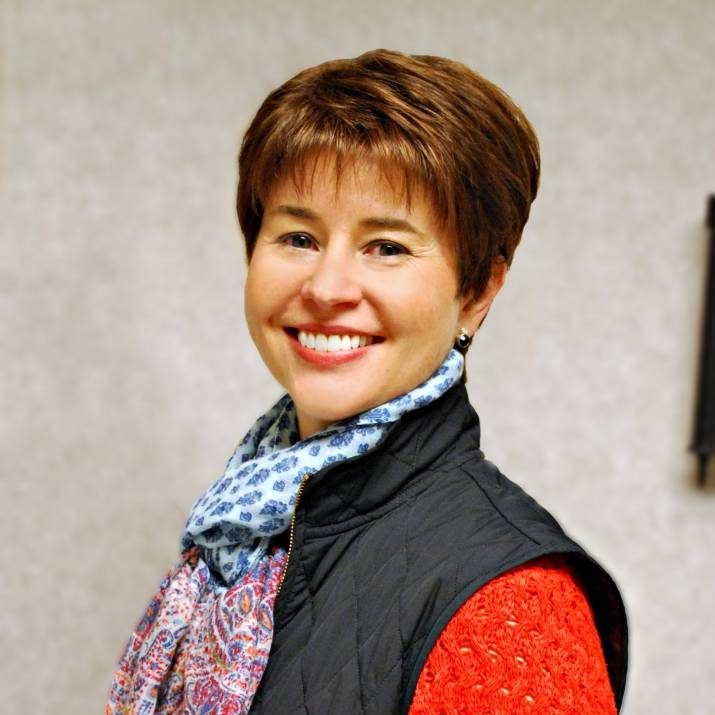 Woman with short brown hair smiling with scarf and vest on