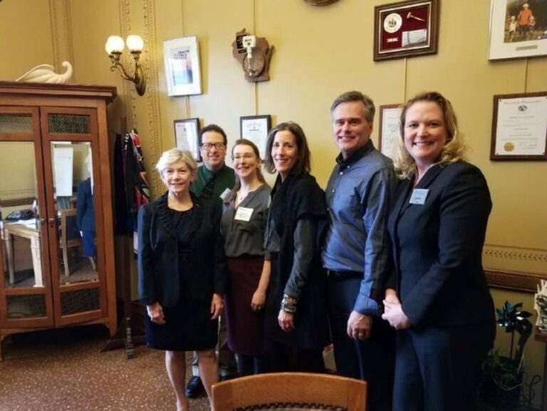 Employees posing with Janet Bewley in office with plaques on wall