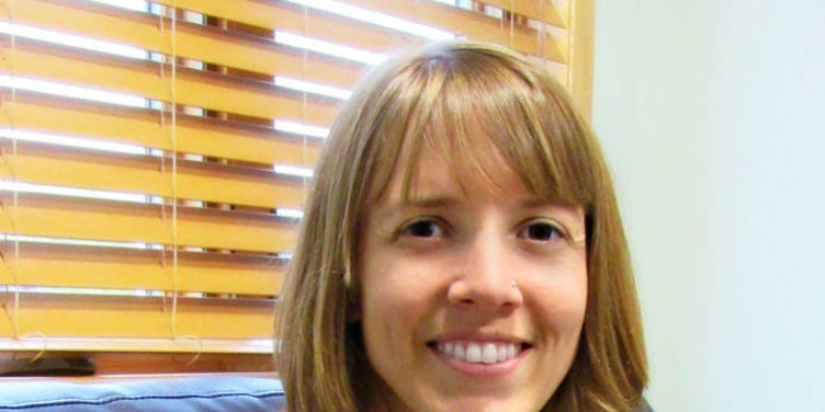 Woman smiling with short dirty blonde hair and bangs, sitting on couch