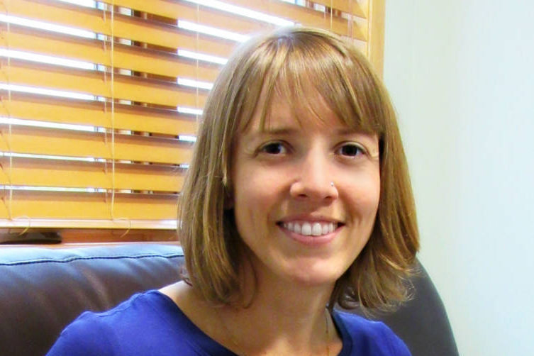 Woman smiling with short dirty blonde hair and bangs, sitting on couch