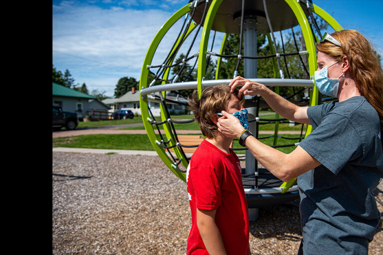 Woman with mask on adjusting her son's mask
