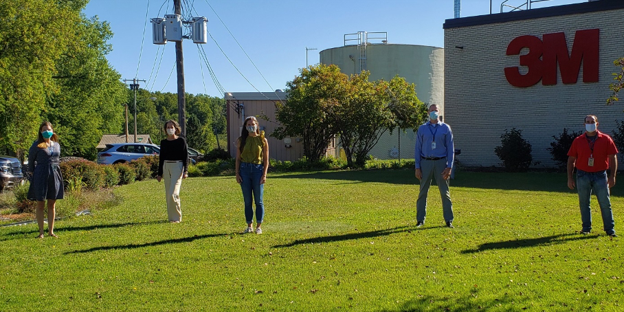 Staff members standing outside and wearing face masks, standing far apart from one another