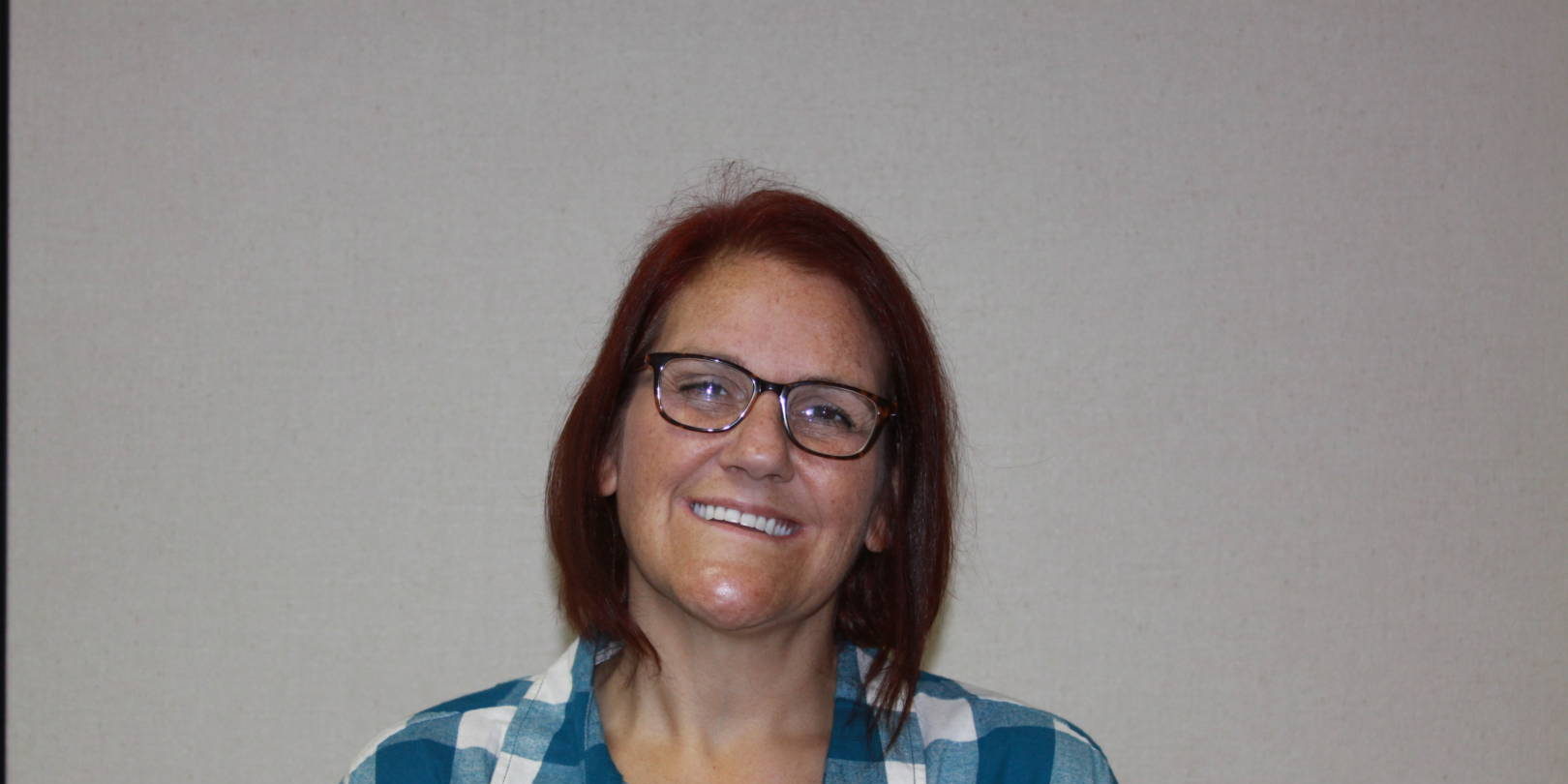 IMG_9141 Woman smiling with dark red hair, glasses, and blue and white plaid shirt