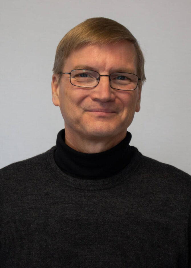 Headshot of man with glass and turtleneck sweater