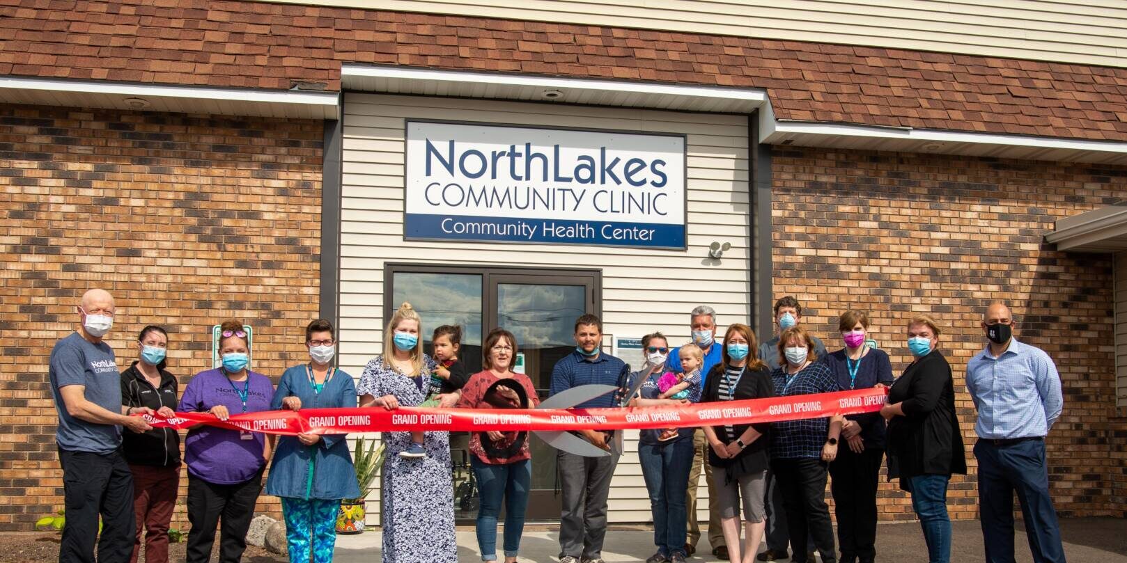 Staff outside of Hurley clinic building using giant scissors to cut a red ribbon