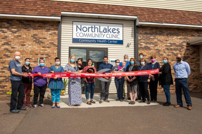 Staff outside of Hurley clinic building using giant scissors to cut a red ribbon