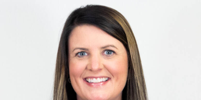 Headshot of woman with straight shoulder length brown hair and highlights, smiling at camera with patterned top