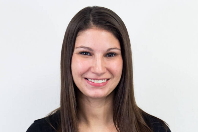 Torso-up shot of woman with dark brown straight hair and striped t-shirt, smiling at camera