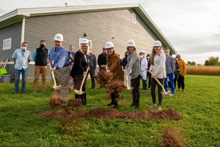 Staff members outside of Turtle Lake clinic building with hard hats, shoveling dirt
