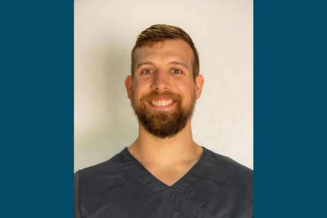 Benjamin-Tenpas-1080×720 Headshot of man with dark gray scrub top and beard, smiling