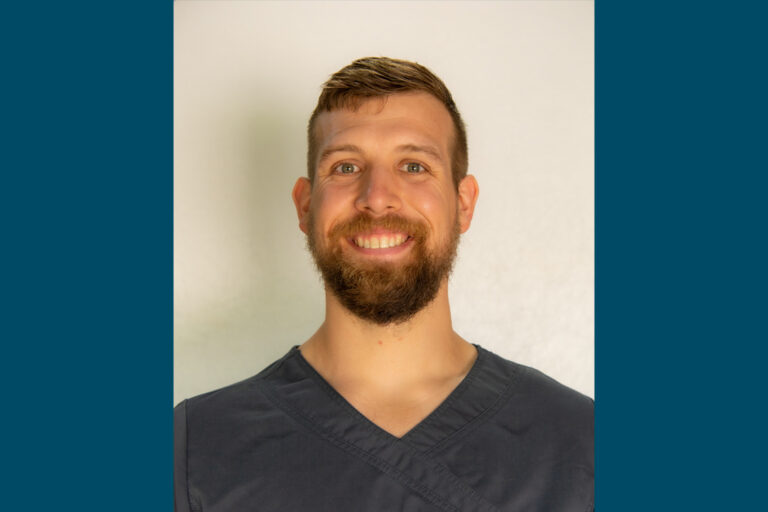 Headshot of man with dark gray scrub top and beard, smiling