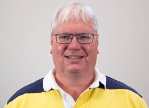 Headshot of man with white hair, square glasses, and yellow and blue striped polo