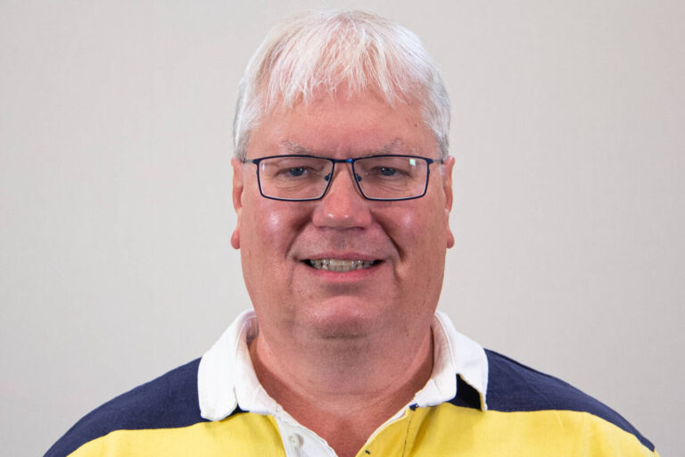 Headshot of man with white hair, square glasses, and yellow and blue striped polo