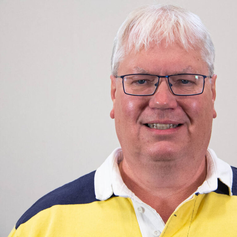 Headshot of man with white hair, square glasses, and yellow and blue striped polo