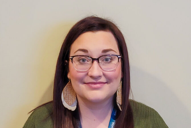 Headshot of woman with dark brown/red hair and glasses with large earrings