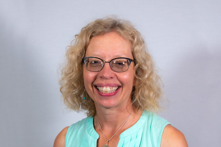 Headshot of woman with blond curly haired woman with light blue tank top