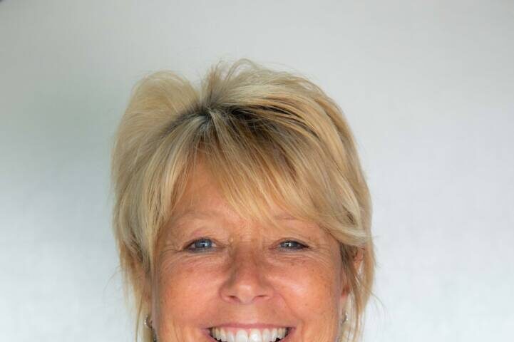 Headshot of woman with blonde ponytail smiling at camera with white and purple bright floral top