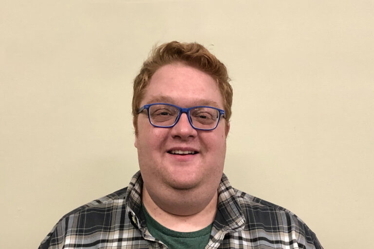 Headshot of man with blue hair and plaid top
