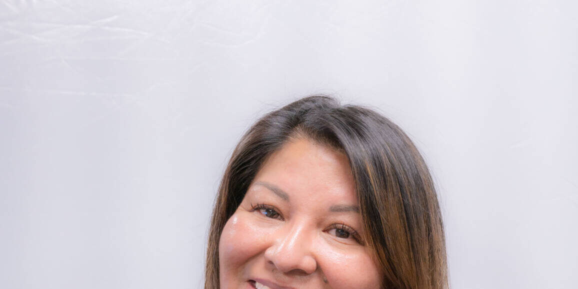 Headshot of woman, tilted head with ruffled blue top and straight brown hair with highlights