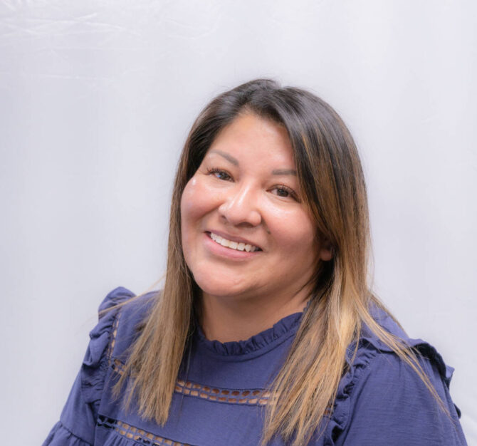 Headshot of woman, tilted head with ruffled blue top and straight brown hair with highlights