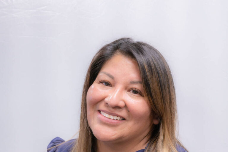 Headshot of woman, tilted head with ruffled blue top and straight brown hair with highlights