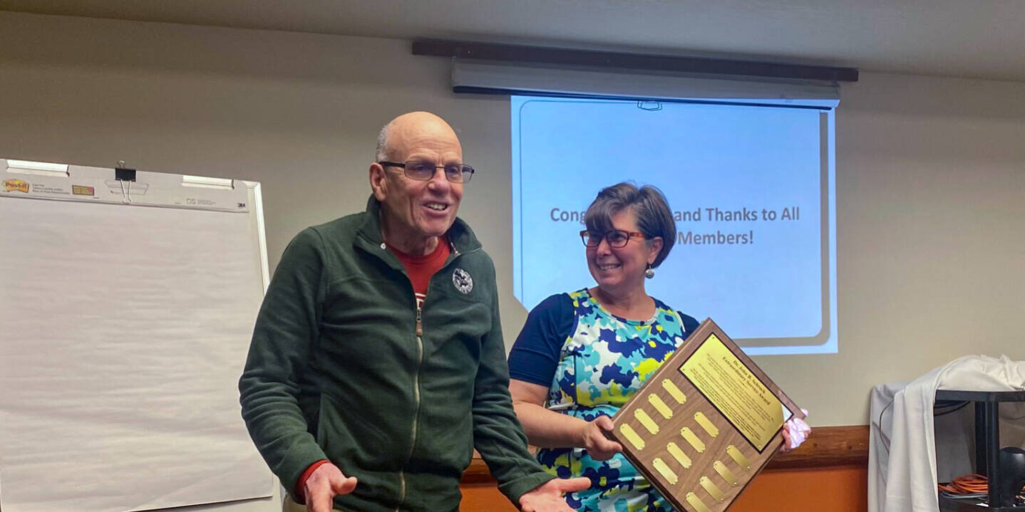 Dr. Schrock smiling in front of projecter presentation