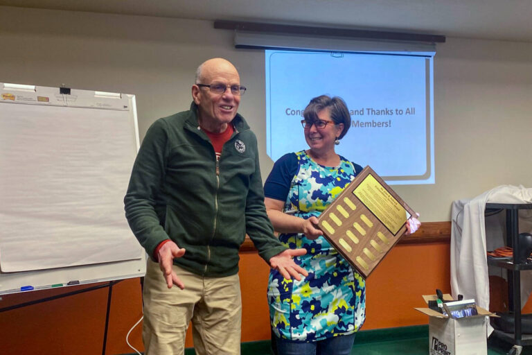 Dr. Schrock smiling in front of projecter presentation