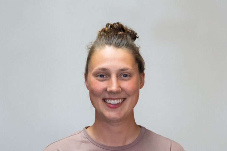 Headshot of woman with light brown shirt and messy bun