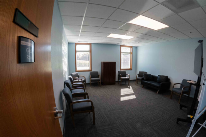 Turtle-Lake-Clinic-Group-Room Carpeted office room with chairs along the walls