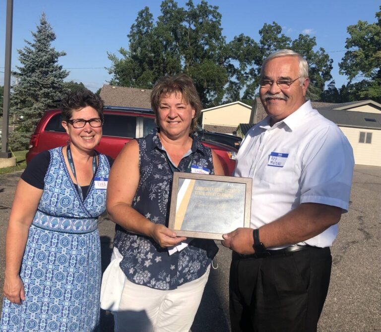 3 people posed and holding a "Community Health Center State Grant Champion" frame