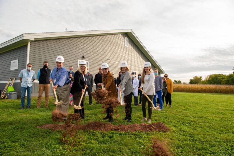 Staff members with hard hats and shovels digging in dirt in front the clinic