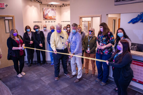 Staff members in face coverings cutting yellow ribbon in optometry office