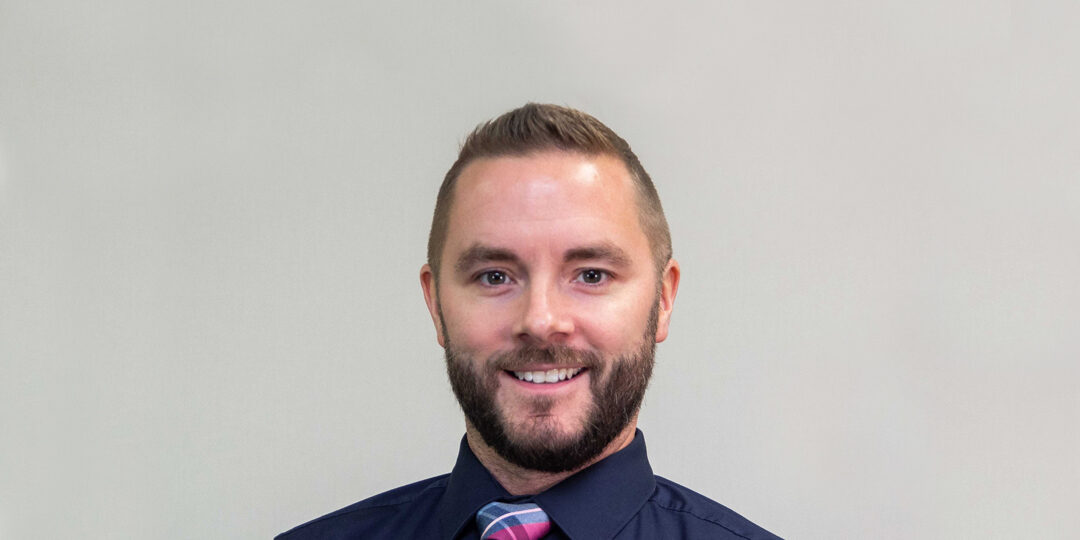 Geoffrey-Holloway-Featured-Image headshot of man with short hair, beard, and dark blue shirt with bright pink and blue tie