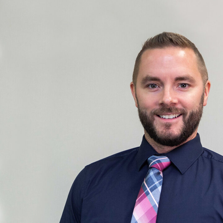 Geoffrey-Holloway-Featured-Image headshot of man with short hair, beard, and dark blue shirt with bright pink and blue tie