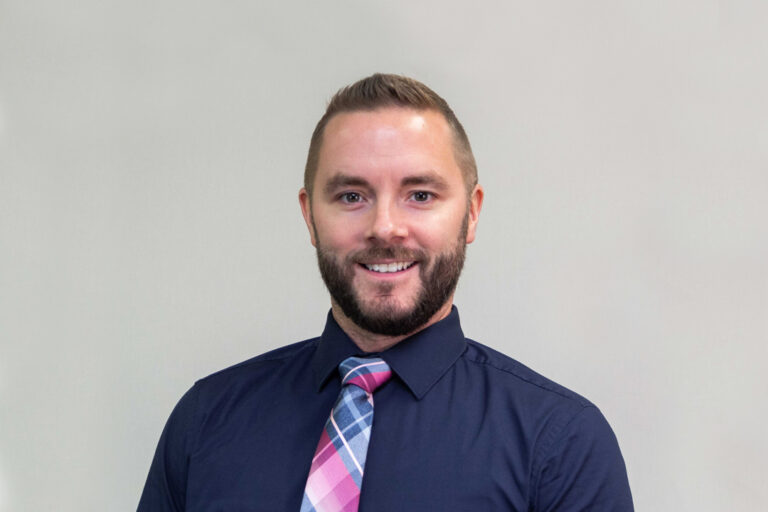 headshot of man with short hair, beard, and dark blue shirt with bright pink and blue tie