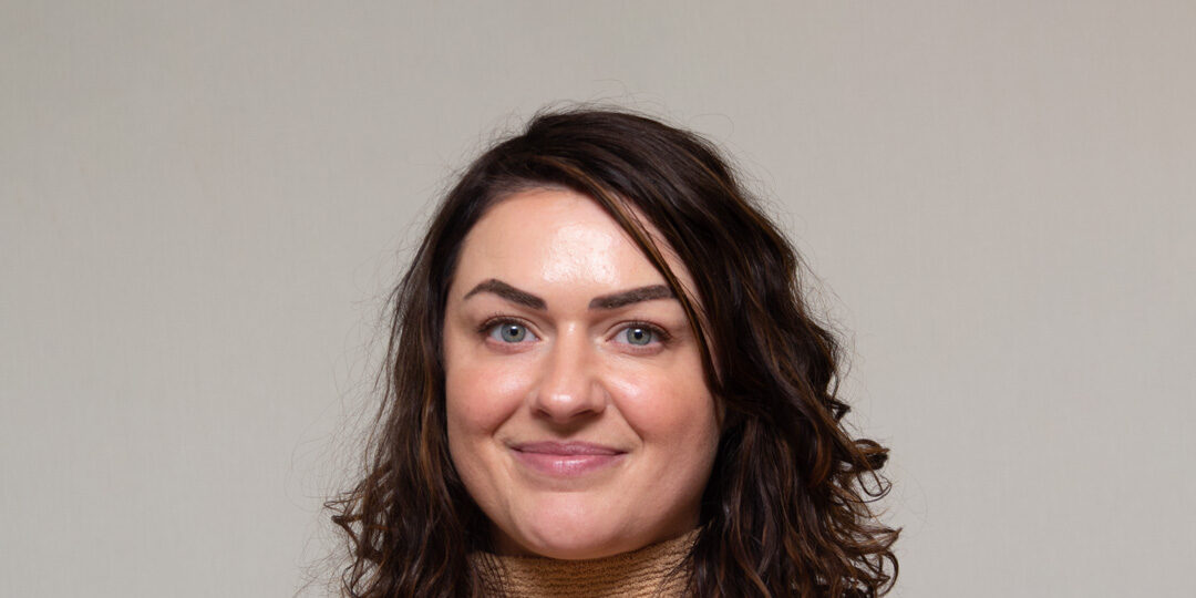 Headshot of woman with shoulder length brown hair and tan turtleneck