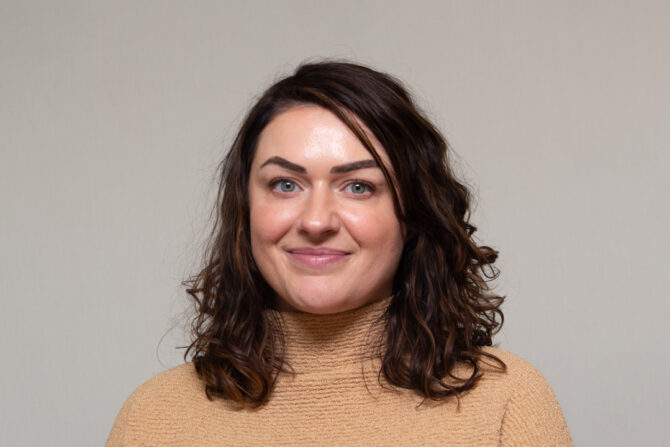 Headshot of woman with shoulder length brown hair and tan turtleneck