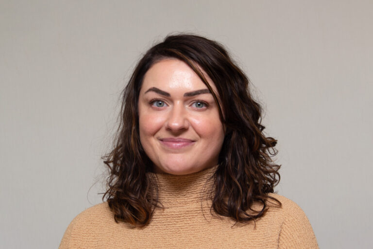Headshot of woman with shoulder length brown hair and tan turtleneck