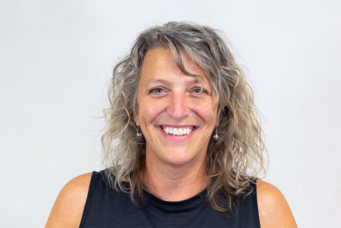 Woman with shoulder length curly light hair and black tank top