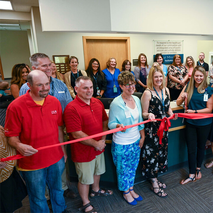 Cumberland-Ribbon-Cutting-Ceremony-Featured-Image Large group of men and women standing and holding a red ribbon in a clinic lobby